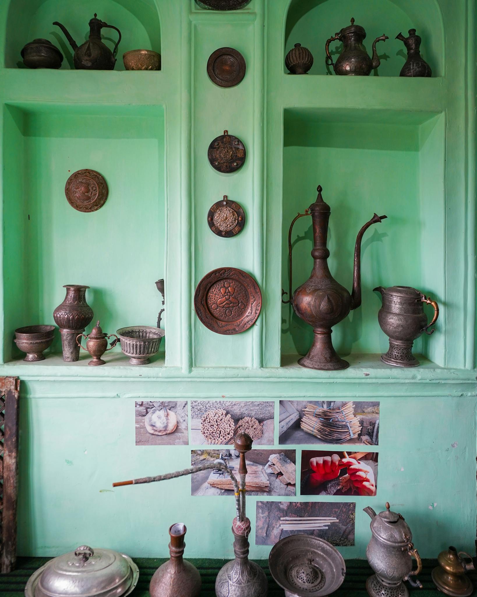 A collection of vintage metal pottery and utensils on a mint green storage shelf, adding historical charm.