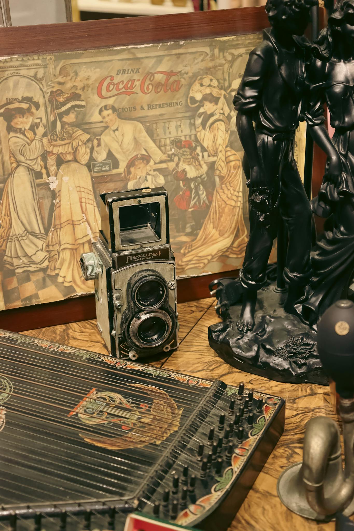 An assortment of vintage antiques featuring an old camera, figurines, and a Coca-Cola advertisement.